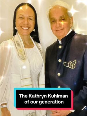 The cover image features two people posing together in a well-lit setting. On the left, a woman smiles at the camera, wearing a white dress and a white scarf with golden details. On the right, a man with white hair is wearing a dark navy jacket with a crest. Below them, a text overlay reads, 'The Kathryn Kuhlman of our generation'.