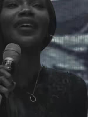 A black and white close-up photo shows a woman singing with a microphone. The background has abstract blurry shapes.