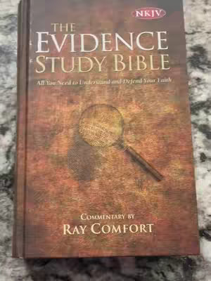 The cover of a book, titled "The Evidence Study Bible" is displayed. The image has a dark, textured background reminiscent of aged paper. A large magnifying glass is superimposed over the center of the cover. The book's title, along with the author's name, "Ray Comfort", is also visible.