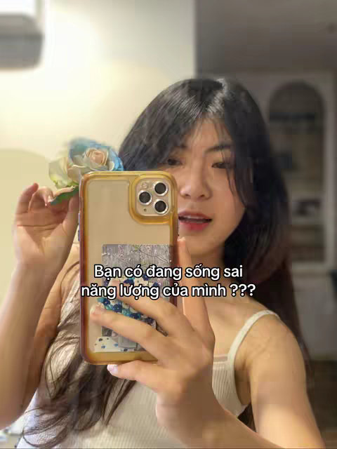 A woman is holding a phone with text overlaid on the screen. She is facing the camera. She is indoors, and the background is blurred.