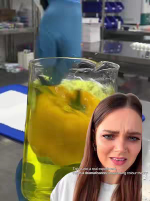 The cover image captures a woman with a surprised expression. The background features a lab-like setting with visible equipment and colorful liquids in a beaker held by a person with blue gloves. The woman's face is overlaid on the image. A text overlay informs about a dramatization regarding color theory.