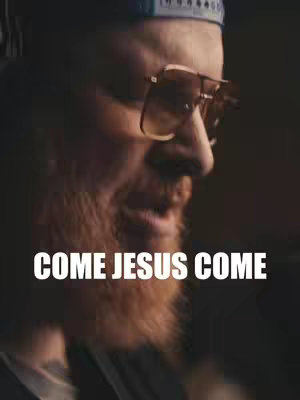 The cover image features a close-up shot of a man's face. He appears to be looking down and to the left, with a small portion of a cap visible on his head. He is wearing sunglasses, and the background is dark, causing the man's face to be the main focus. White text that reads 'COME JESUS COME' is overlaid at the bottom.