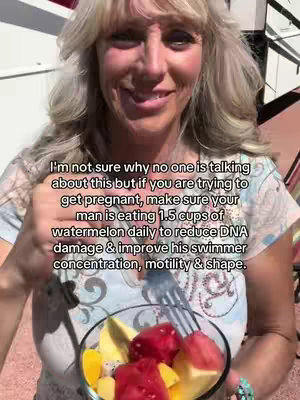 A woman with blonde hair and a light colored top holds a clear bowl containing a fruit salad, looking towards the camera with a slight smile. Overlayed text provides information about fertility foods and the importance of a man's diet when trying to conceive. The background is somewhat blurred suggesting an outdoor setting.