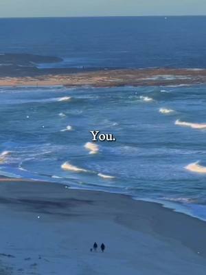 A scenic image with a beach and ocean under a light sky. The beach, in the foreground, has a gentle slope with two shadowy figures walking together, suggesting a couple or friends. The ocean has moderate waves, with a visible horizon. The overall composition evokes a sense of calm and open space.