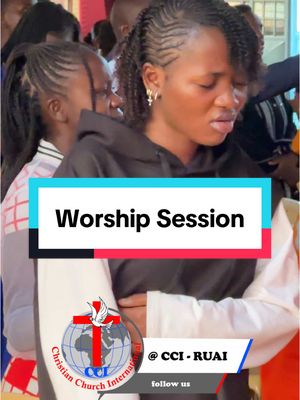 The image shows a medium shot during a worship session, filled with people. A woman with braided hair stands close to another person. All their faces seem to be in the praying position. The background looks like an event or a meeting hall.