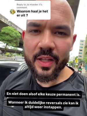 A man with a bald head and a beard is speaking directly to the camera, likely outdoors near a street. He is wearing a black shirt, and there is text overlayed on the image; in the top left is a comment from another person asking a clarification and at the bottom there is a commentary.