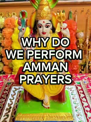 A statue of a Hindu deity, possibly Amman, is the central focus, adorned in a yellow sari and gold jewelry, seated on a red platform against a backdrop of orange and gold colors with floral arrangements. Text overlayed in white on the statue.