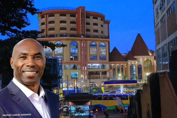 A promotional image featuring a man in a suit with a large, modern building in the background. The man is smiling, and the background includes a tall building, a church-like structure, and various vehicles, indicating a city or urban environment. The time of day appears to be dusk or evening due to the blue sky.