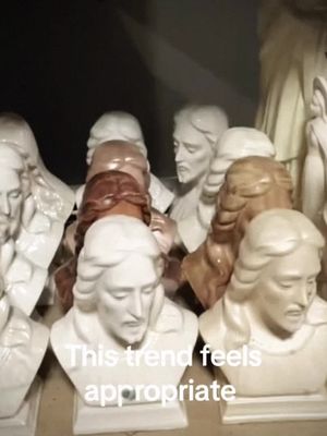 The image shows a collection of busts of Jesus, arranged in a close-up shot. The busts vary in color from white to brown, and are illuminated with a soft lighting. Text overlay at the bottom of the frame reads, 'This trend feels appropriate.'