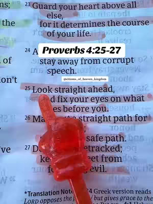 The image is a close-up of a page from a book, likely a Bible, with text highlighted and a red, plastic hand or pointer placed over the text. The text is referencing Proverbs 4:25-27. The background is a mix of white and yellowed paper, with visible text underneath. The red object in the foreground adds vibrant color to the composed image.