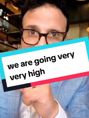 A man wearing glasses is centered in the frame, with a blue blazer. A horizontal, rectangular text box is overlaid on the bottom third of the frame, containing the words 'we are going very very high'. The background is a muted, blurred view of what appears to be an indoor setting, likely a restaurant or bar, indicated by objects that are partially visible behind the man.
