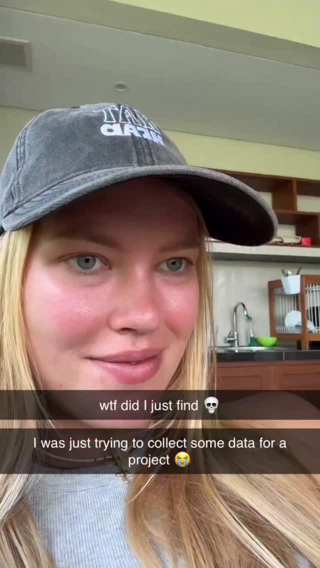 A woman with blonde hair and a grey baseball cap is looking at the camera. Her skin is flushed, and she is wearing a grey top. Text overlays on the image read, 'wtf did I just find 💀 I was just trying to collect some data for a project 🥺'. The background is a kitchen setting.