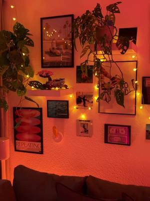 A wall decorated with framed photos, plants, and string lights against a warmly lit, orange-toned background.