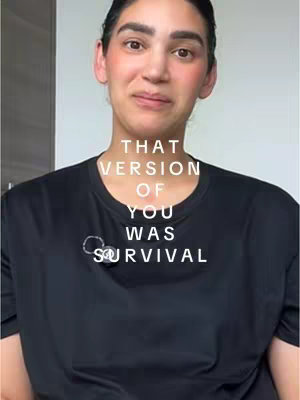 A selfie-style video cover featuring a woman looking directly at the camera. Text is overlaid on the image in a vertical stack, reading "THAT VERSION OF YOU WAS SURVIVAL". The woman has dark hair pulled back, fair skin with visible blush, and is wearing a black t-shirt. The background appears to be a simple white wall or surface, keeping focus on her and the text.