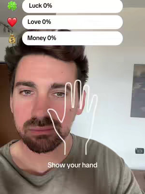 A selfie-style image featuring a man with a brown beard and short, dark hair. He is positioned in the center, and the background appears to be a room with a window and a blank wall. The focus is primarily on his face and upper body.