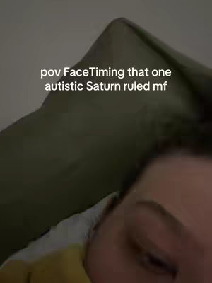 The image shows a close-up of a person's face and part of a pillow. The person is lying down, with the camera angle from above and to the side, focusing on the person's eye area. The pillow takes up the majority of the frame, and the background is a soft, dark color. Text overlaid on the image reads, "pov FaceTiming that one autistic Saturn ruled mf."