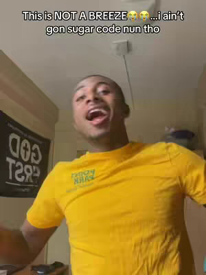 A young Black man with an open mouth and eyes looking up, possibly singing or speaking emphatically. He is wearing a yellow shirt with a green logo and is indoors. The background is blurry with some signs of the person's room. Text is overlaid at the top.