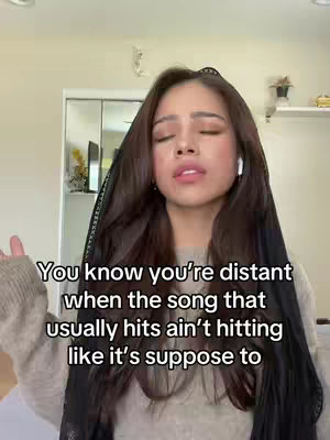 A young woman with long brown hair, wearing a beige sweater and a black head covering, is looking up with a subtle expression. Text overlayed over the image.