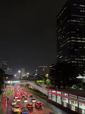 A nighttime cityscape with a multilane highway filled with car headlights, a tall high-rise building illuminated, and overall darkness.