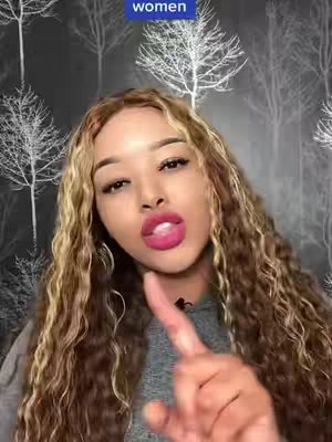 A woman with long, wavy blonde and brown hair looks directly at the camera with a serious expression, pointing with her right index finger. She has full pink lipstick. A blue rectangular text box is above her head, and the background is a repeating pattern of stylized trees on a dark background.