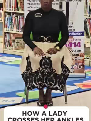 A woman sits on a chair in a library or classroom setting. The background includes bookshelves. She wears a black top, a beige skirt with black lace detailing at the hem, and black shoes. The text overlay at the bottom states, "HOW A LADY CROSSES HER ANKLES".