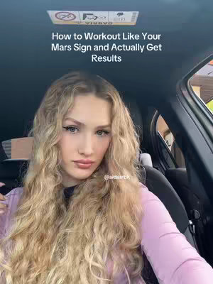 A selfie taken in the front seat of a car. A young woman with long, wavy blonde hair looking at the camera. She's wearing a pale pink top. Text overlayed at the top says, 'How to Workout Like Your Mars Sign and Actually Get Results'.