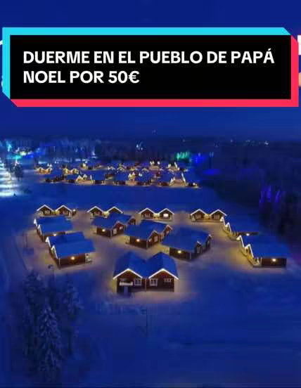 An aerial view of a snowy village at dusk. Small, illuminated wooden houses are clustered together with snow-covered surroundings and a dark blue sky. A rectangular banner with text overlays across the center.
