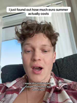 A selfie-style shot with the creator in the center. The creator has curly brown hair, and is wearing a red and white checkered shirt over a white undershirt. Behind them are what appear to be white curtains or blinds. The creator's face is in the middle of the image, conveying a surprised or open-mouthed expression. Text overlays in white font are added to the top and bottom of the image.