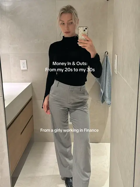 The cover image shows a well-lit bathroom setting with a female figure taking a selfie. The person, dressed in a black turtleneck and gray trousers, is holding a phone, capturing the mirror image. The background includes a clean white sink area and a towel rack. Text overlays on the image read "Money In & Outs: From my 20s to my 30s" and "From a girly working in Finance."