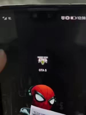 The image displays a smartphone screen showing the GTA 5 mobile game icon. Below the screen, the red and black head of a Spider-Man figure is visible.