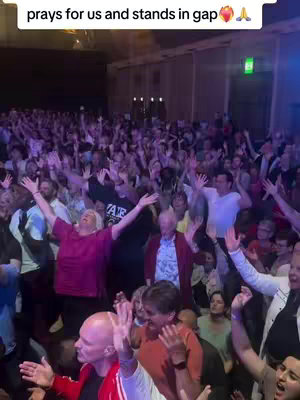 A video cover image shows a large crowd in an auditorium with raised hands. The lighting is dim with blue hues, likely during a performance or service. Text overlaid at the top reads "prays for us and stands in gap." Various people are visible across the audience, with diverse attire and ages.