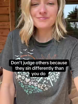 A woman with blonde hair is facing the camera in this selfie style image. She is wearing a grey t-shirt with a design that features different colored leaf-like shapes. The text on the screen is superimposed on top of the image