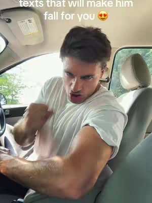 A man is in the driver's seat of a car, leaning towards the camera with a tense expression, seemingly flexing his arm. The overhead light is on, and the inside of the car is visible.