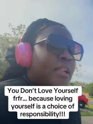 A person wearing large black sunglasses, pink headphones, and a black outfit speaks to the camera. Text overlayed at the bottom reads: "You Don't Love Yourself frfr... because loving yourself is a choice of responsibility!!!"