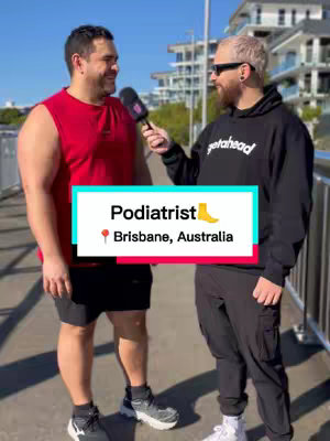 Two men are standing outside, facing each other and seemingly engaged in a conversation. The man on the left wears a red sleeveless shirt and shorts. The man holds a microphone. On the right, a man with a black hoodie that has white writing on the chest, and is wearing sunglasses. A text overlay near the bottom reads 'Podiatrist' and cites a location in Brisbane, Australia.