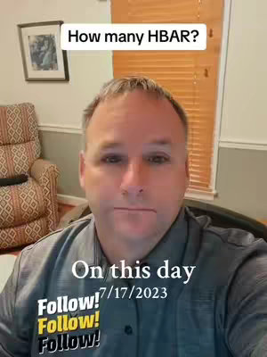 A man is centered in the frame, facing the camera. He has short brown hair and is wearing a gray collared shirt. The background includes a window with blinds and a framed picture. Text overlays include "How many HBAR?" and "On this day".