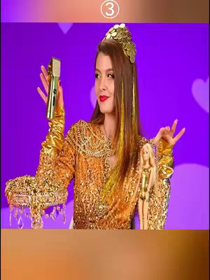 A woman, posed in a golden, shimmering gown, holds a gold microphone in one hand and makes a hand gesture as if casting a spell, a Barbie doll with a matching golden outfit and a tiara is positioned on the right side of the composition, all set against a vibrant purple backdrop dotted with white hearts.