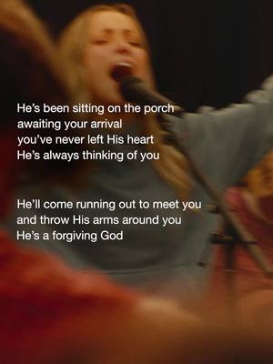 The blurry image shows a woman with long blonde hair, singing with her mouth open towards a microphone. The atmosphere is dark, but the woman is being illuminated, perhaps by stage lights. Above the woman is the text: "He's been sitting on the porch awaiting your arrival, you've never left His heart, He's always thinking of you. He'll come running out to meet you and throw His arms around you, He's a forgiving God."