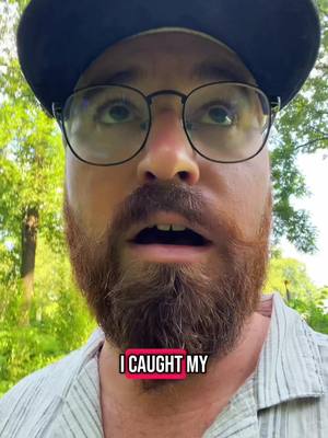 A close-up shot of a man with a surprised expression, looking upwards. He has a full, reddish-brown beard, glasses, and a dark baseball cap, the text overlayed on top. Background is blurred with green foliage.