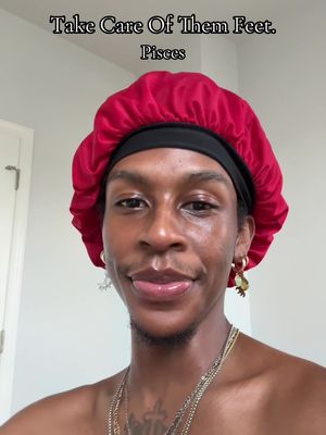 A selfie-style portrait of a person wearing a red satin bonnet. The person has dark skin, a small mustache, and is wearing several necklaces and hoop earrings. Text overlays the image.