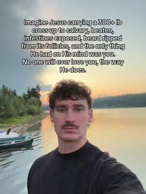 A man with short, curly dark hair and a mustache stands in front of a lake at sunset. The sky is filled with orange and yellow hues, and the water reflects the colors. A small boat is docked to the left, and trees line the distant shore. The man is wearing a black shirt and looking directly at the camera. Text overlayed the image.