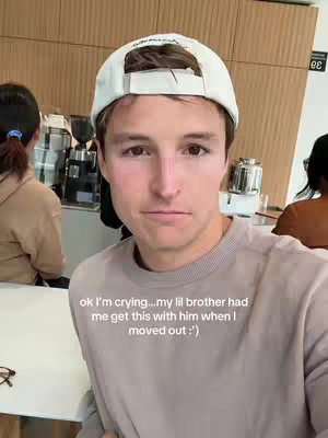 A young man in a white baseball cap and a light brown sweater looks directly at the camera with a slightly somber expression, and text is overlaid at the bottom of the frame.
