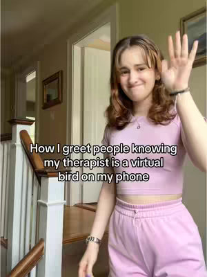 A woman stands in a well-lit hallway, smiling and waving at the camera. She is wearing a pink crop top and matching sweatpants, and there is text overlayed on the image.