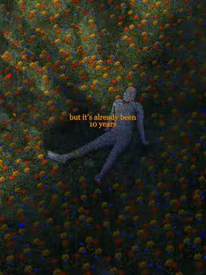 An artistic, top-down view presents a figure lying in a vibrant field of flowers. The figure, rendered in a muted, almost stone-like texture, is positioned amidst a dense arrangement of colorful blooms including red, yellow, and blue flowers. The image has a soft, dreamlike quality, with a light, airy feel, suggesting a scene of introspection or contemplation.