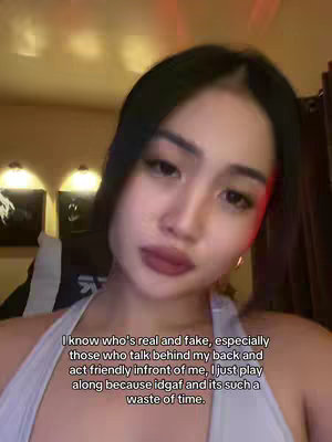 A young woman with dark hair and a light-colored top is the focus of a selfie-style video cover image. The background is warm-toned, possibly lit by soft lighting. Text is overlaid on the image in simple white font.