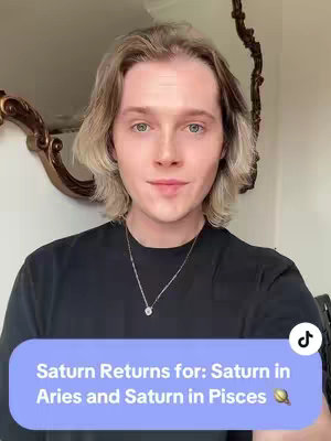 A young man poses in front of a mirror, his face centered in the frame. He has light eyes, blonde hair, and is wearing a black shirt and a silver necklace. A blue rounded rectangle with white text reading 'Saturn Returns for: Saturn in Aries and Saturn in Pisces' covers the lower part of the image, with a gold graphic in the middle of the rectangle. The TikTok logo is visible in the top right corner.
