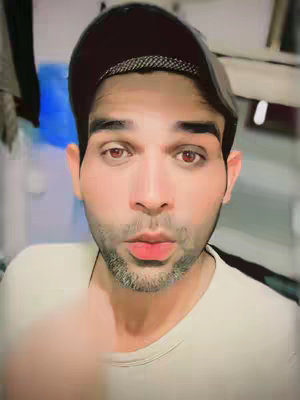 A selfie of a man wearing a baseball cap, with a digitally enhanced face. The man has reddish eyes and a slightly open mouth, and his facial features appear to be smoothed or distorted. A soft, blurred background is visible.