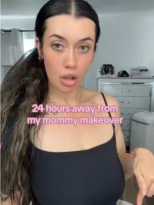 A woman with long dark hair in a ponytail is centered in the frame, her expression open-mouthed. Overlay text in a pinkish-purple gradient reads "24 hours away from my mommy makeover." The background is softly blurred with visible elements of a bedroom.
