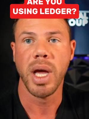 A man with short hair and a beard stares directly at the camera with his mouth open. Above his head is a red banner containing white text. The background is dark and blurry.