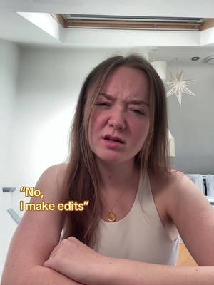 A woman with long brown hair, slightly squinting her eyes and looking upwards with a questioning expression. She is wearing a cream-colored top and a gold pendant necklace. The background is lightly colored and out of focus with an apparent window behind her and something hanging from the ceiling. Text overlays read "No, I make edits".